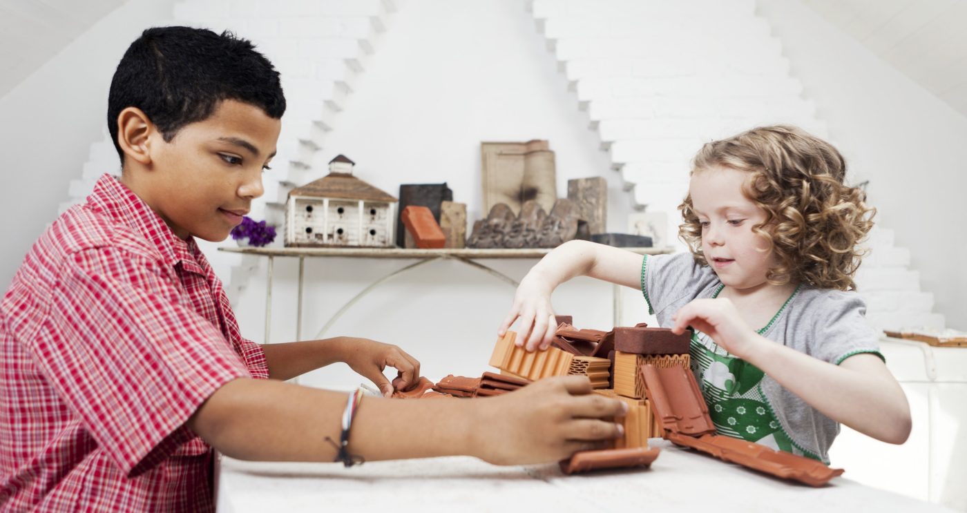 Boy and girl playing with miniature bricks, clay blocks and clay roof tiles in attic loft