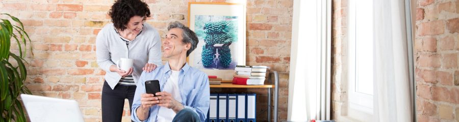 Man with phone in conversatuion with woman in front of brick-lined wall