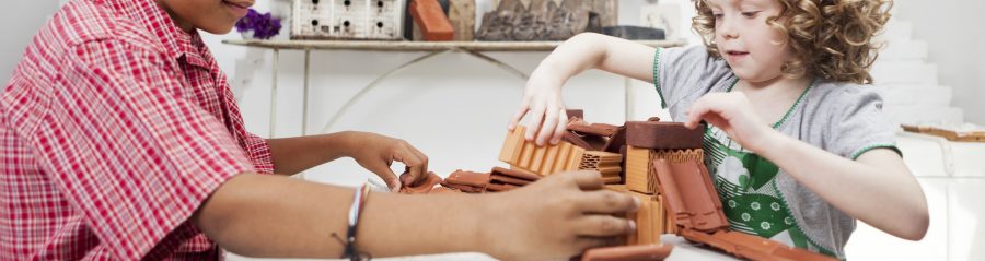 Boy and girl playing with miniature bricks, clay blocks and clay roof tiles in attic loft