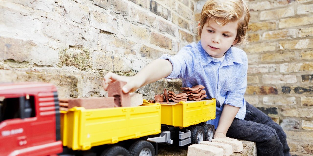 Boy loading miniature bricks and clay roof tiles on toy truck