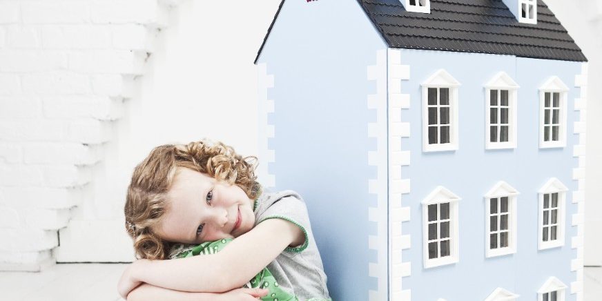 Relaxed and smiling girl sitting next to doll house in attic loft