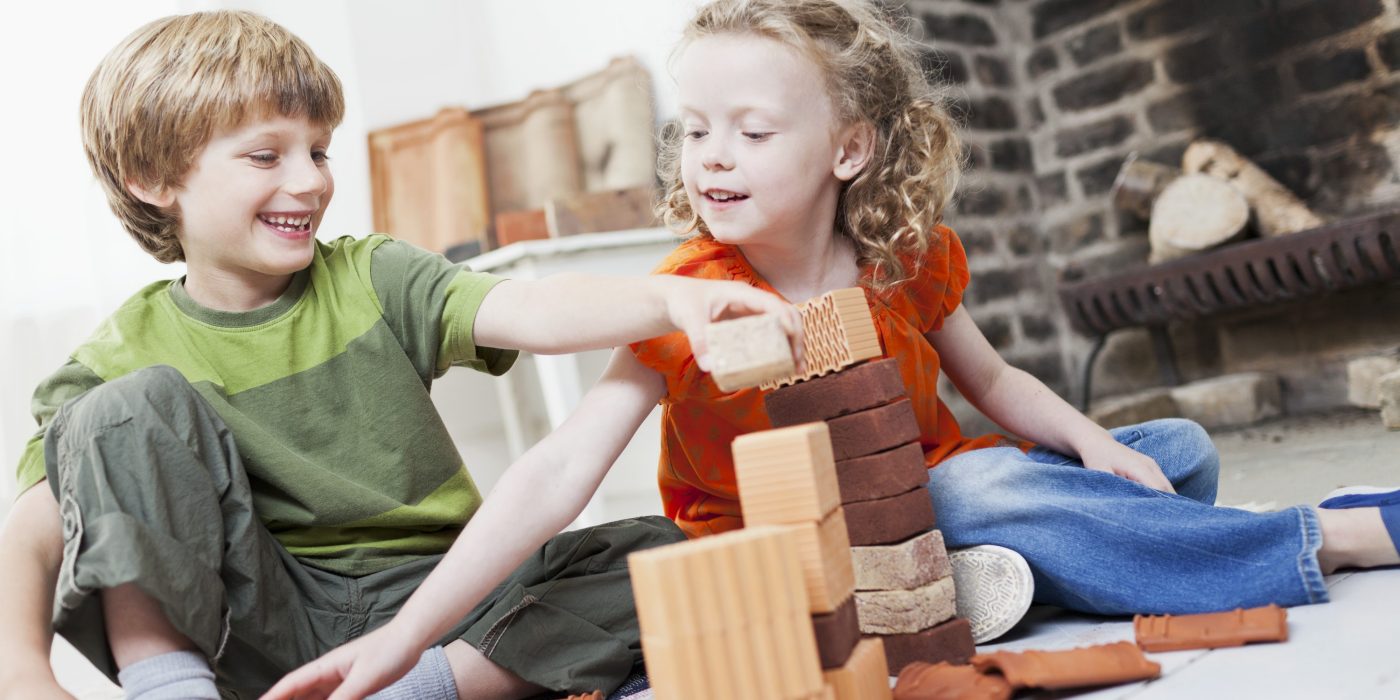Boy and girl playing with miniature bricks, clay blocks and clay roof tiles in front of fireplace